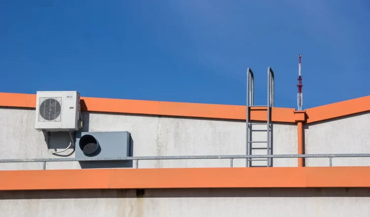 Equipamentos de climatização industrial instalados no topo de um prédio em Curitiba, com unidade externa de ar-condicionado e dutos sobre estrutura metálica, ao céu azul.