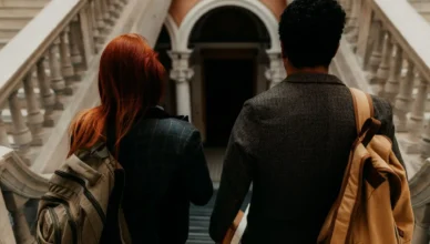 Intercâmbio na Austrália: Guia Completo (Passo a Passo: Casal de intercambistas de costas, com mochilas, subindo escadas em um prédio histórico, olhando para a entrada. Foto que representa intercâmbio na Austrália e preparação para a viagem.